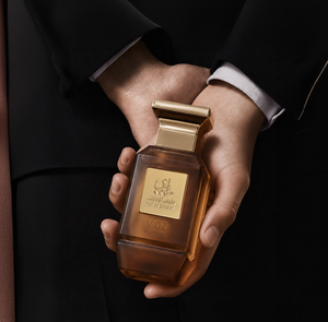 Hands holding V02 unisex perfume bottle 75ml against a dark suit - luxury oud oil in uae