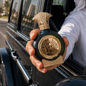 Hand holding YEAR OF ZAYED perfume bottle 75ml from taif al emarat perfumes, throw car window - best tobacco fragrance