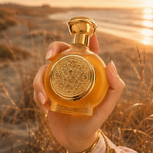 Hand holding GOLDEN OUD unisex perfume bottle 75ml at sunset beach, oud gold perfume