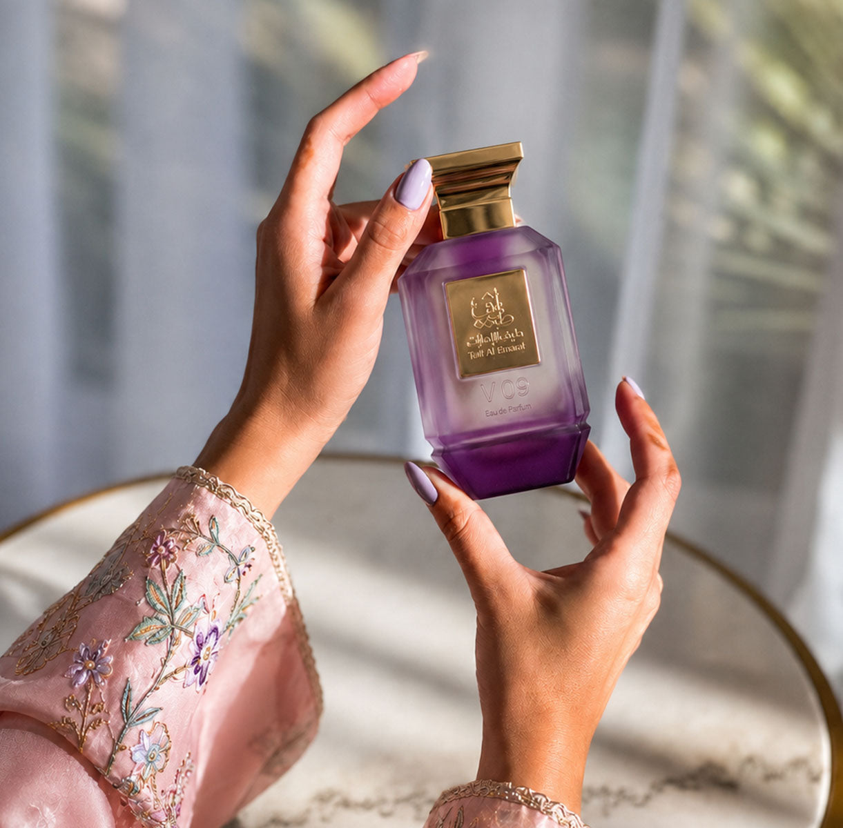 Hands in an embroidered sleeve holding V09 women's perfume bottle 75ml from taif al emarat perfumes - fragrant violet flower fragrance in uae